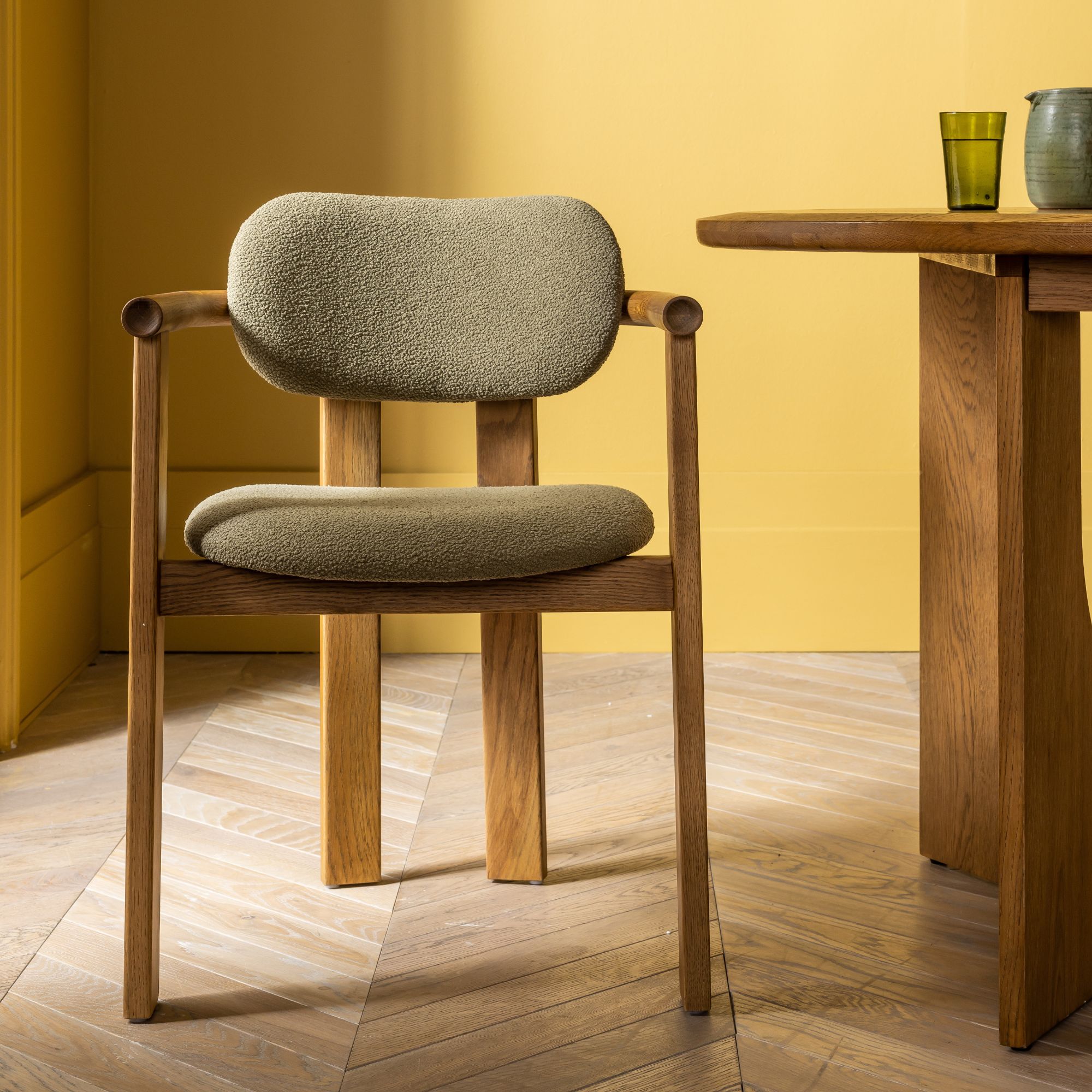 A green boucle dining room chair with wooden accents against a yellow background