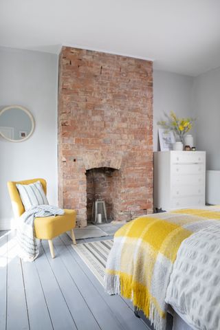 grey painted woof flooring in bedroom with exposed brick fireplace