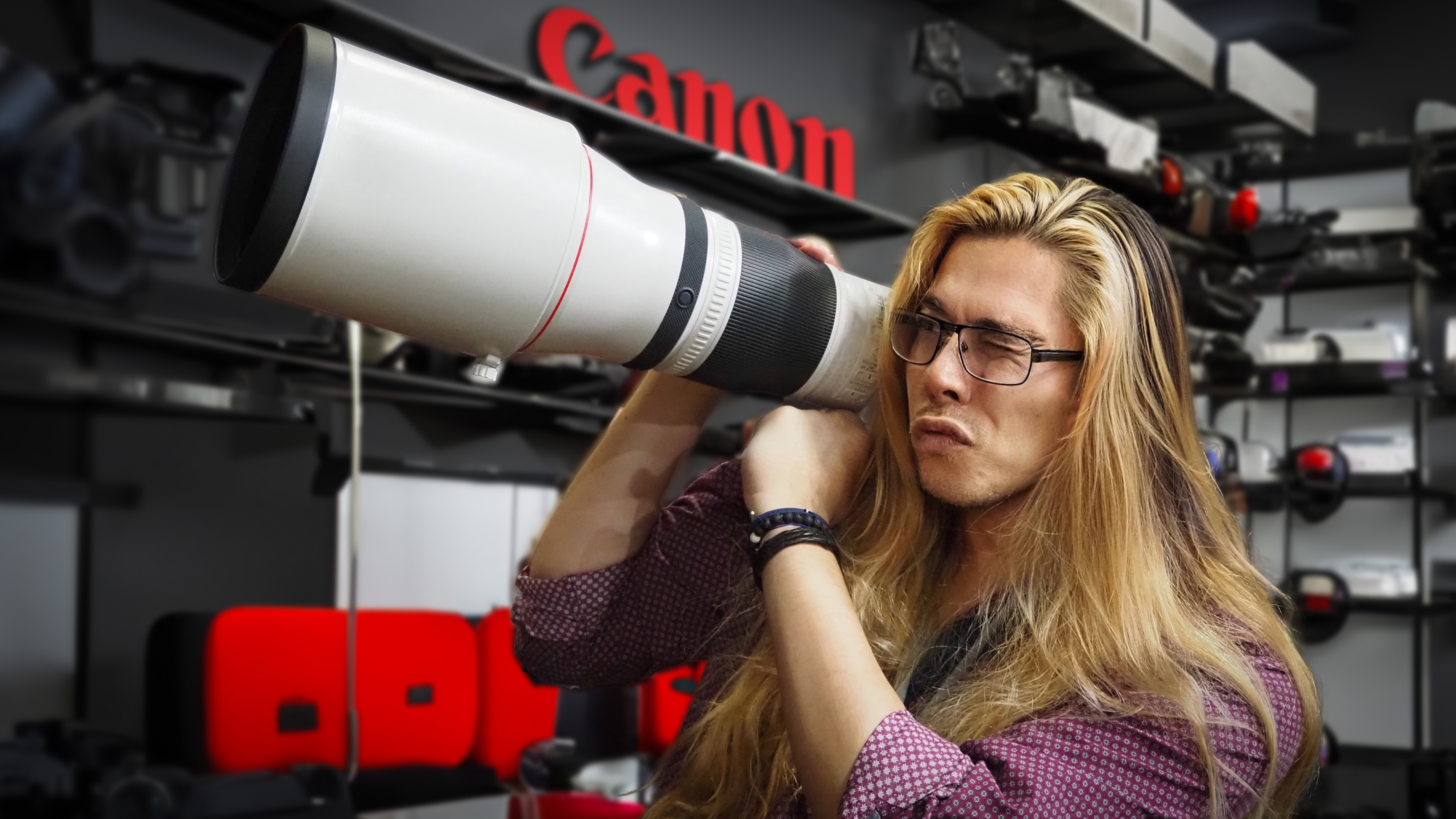 James Artaius holding the Canon RF 600mm f/4 lens like a bazooka, in a shop with the Canon logo in the background