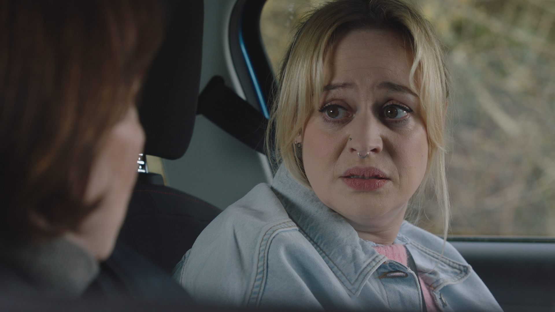 Nicole wearing a denim jacket and looking panicked as she sits in the passenger seat of Siobhan&#039;s car.
