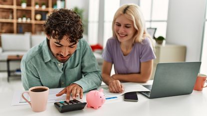 A young couple at a table look at paperwork and a calculator