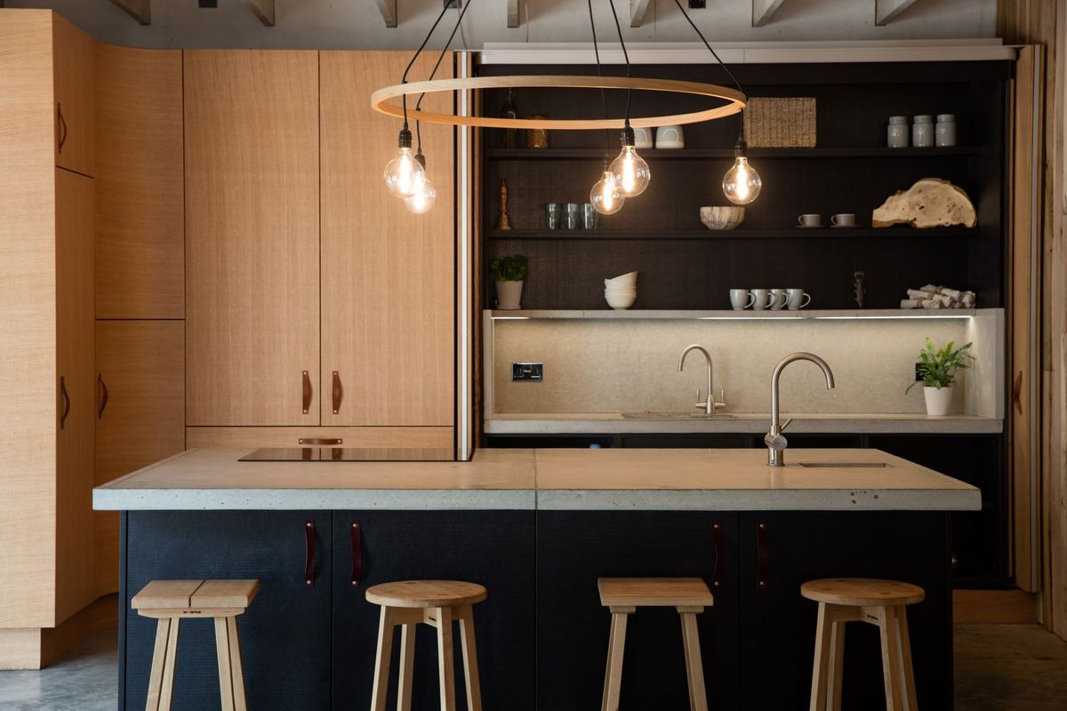 The kitchen has an island and the surrounding surfaces and cupboards are made from wood with a circular timber chandelier above