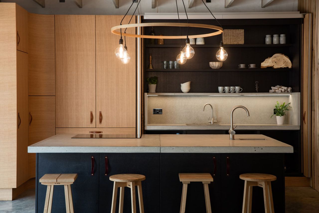 The kitchen has an island and the surrounding surfaces and cupboards are made from wood with a circular timber chandelier above