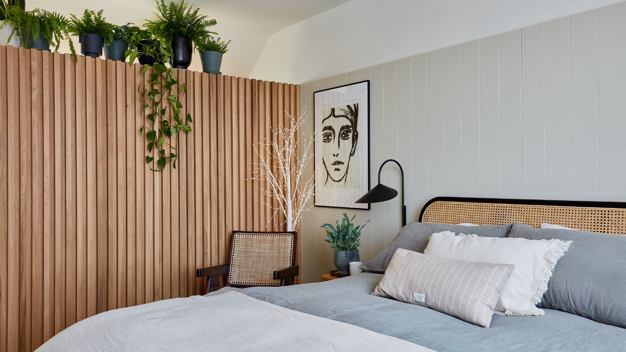 how to decorate a guest room, bedroom with rattan bed, grey bedding, off white tongue and groove, artwork, lamp, chair, wooden panelling on left with plants on top