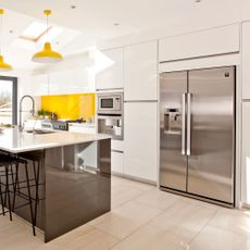 Smart stainless steel American style fridge freezer in a white kitchen with yellow tiled splashback