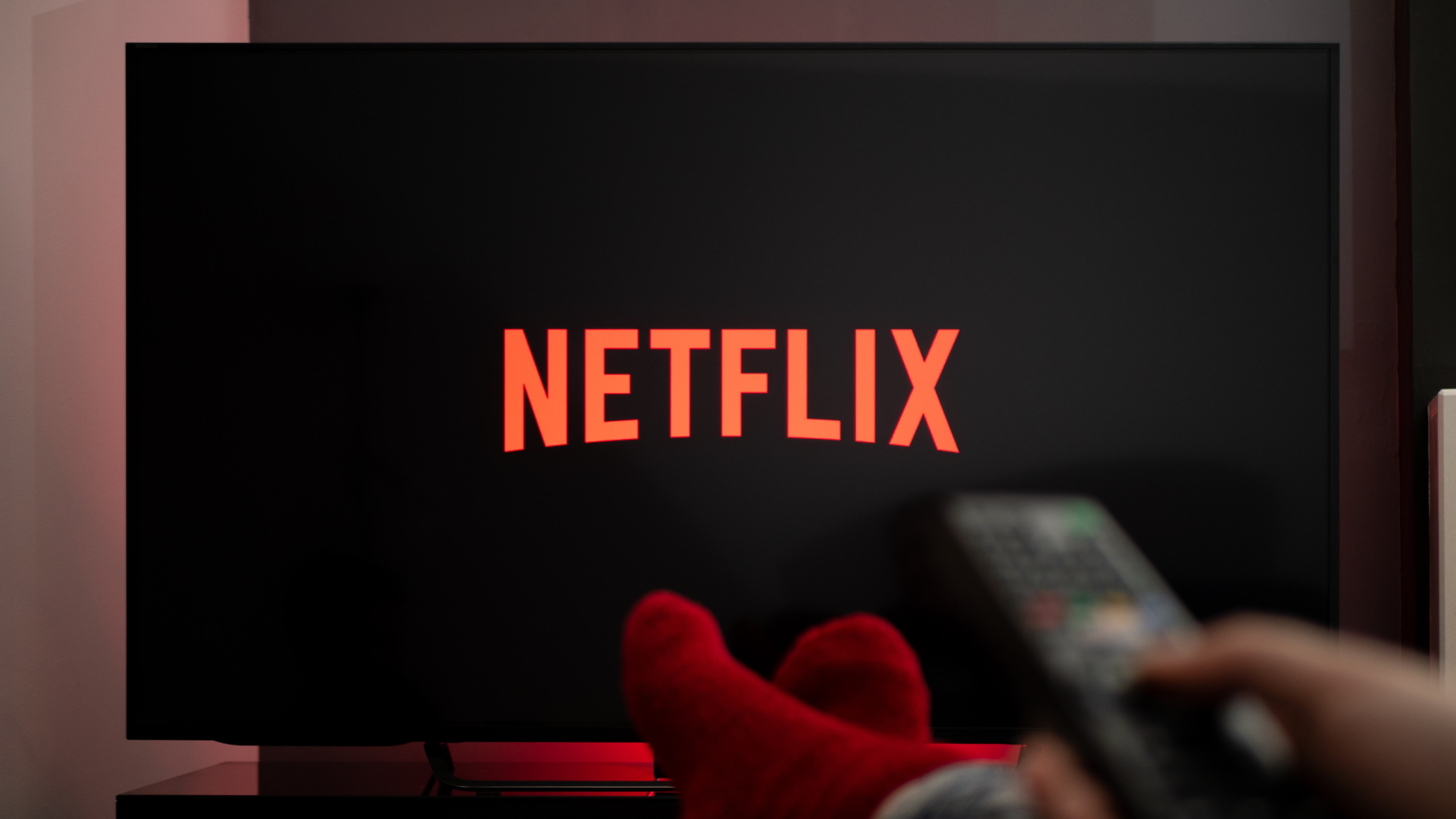 Netflix on TV screen with feet up in front and hand holding remote