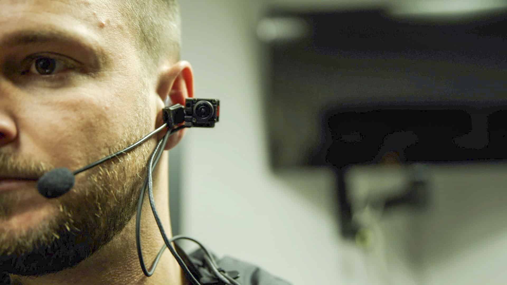 Close-up profile view of a man wearing an ear-mounted compact camera system paired with a headset microphone