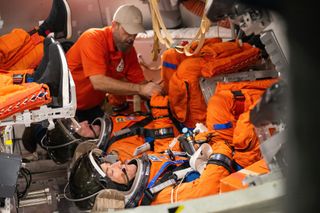 four people in orange flight suits sit in a cone-shaped spacecraft trainer, facing upwards