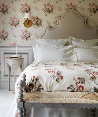 A floral wall behind a grand bed with a neutral baroque-style headboard