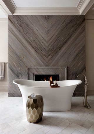 luxury bathroom with freestanding bath and stone fireplace with wood panelling above it and neutral colorscheme