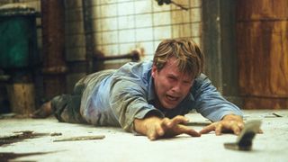 Cary Elwes as Dr. Lawrence Gordon crawls toward a cellphone in a derelict bathroom in Saw