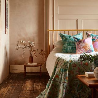 small bedroom colour ideas, plaster coloured walls in bedroom with wooden bed, stool with vase of dried eucalyptus, brightly patterned throw and cushions, artwork, original floorboards