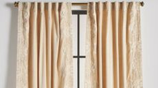 Anthropologie Harlowe curtain panels in Ivory hanging from a decorative brass curtain rod over a tall windowpane. 