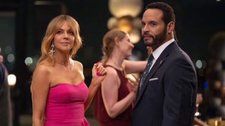 From left to right: Kaitlin Olson as Morgan in a pink dress and holding her right hand up and Daniel Sunjata as Karadec standing next to her in a suit. 