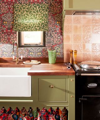 Colorful kitchen with floral patterned wallpaper, blind, green cabinetry, patterned cupboard skirt.