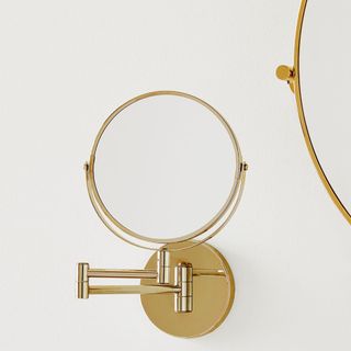 Gold colored mounted makeup mirror next to larger round wall mirror