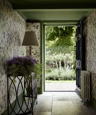 cottage entryway with stone floors, green floral wallpaper and front door open leading into garden