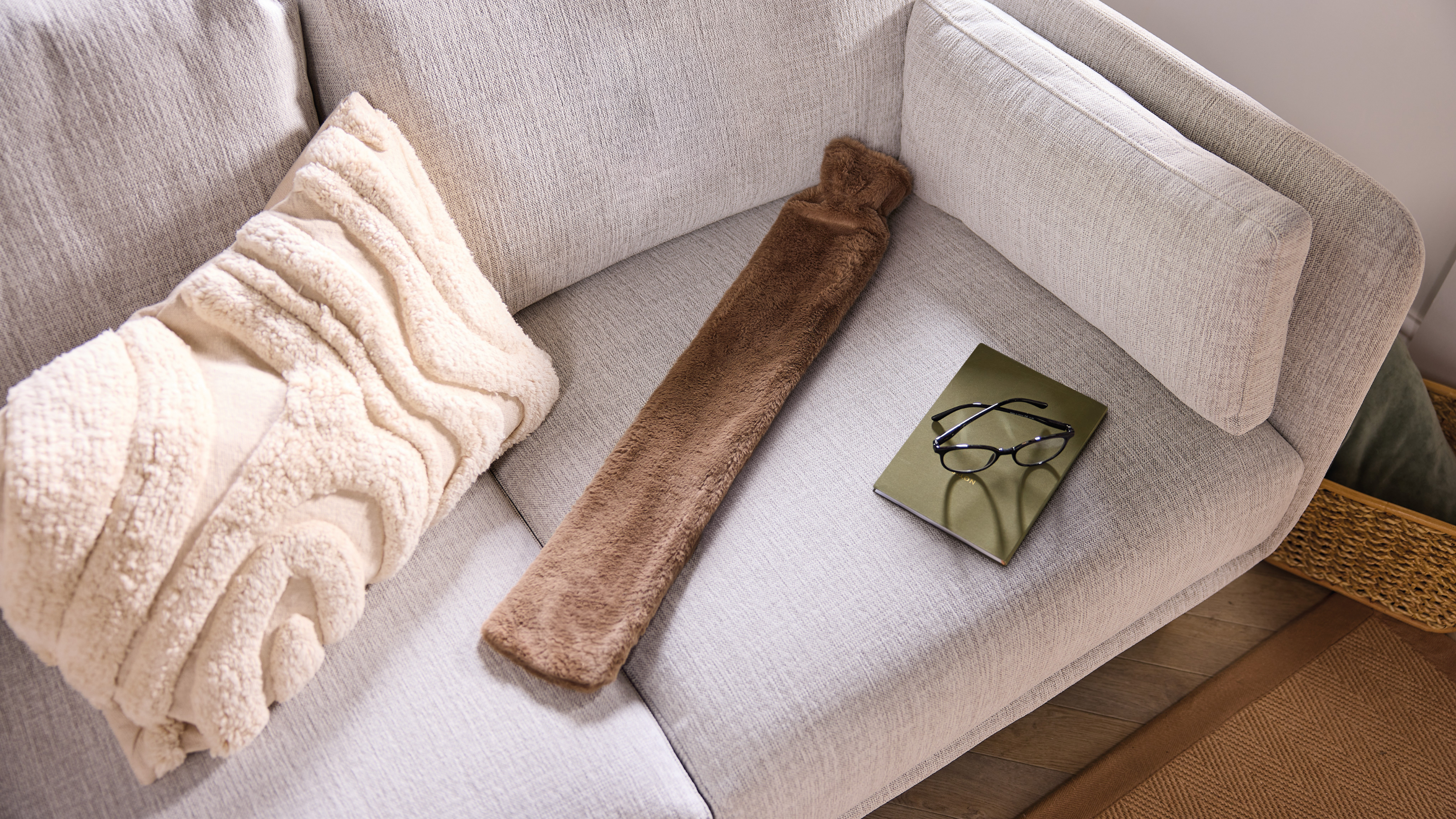 Aldi long hot water bottle in brown on a white sofa.
