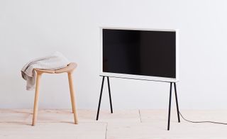 White TV on a black stand beside a wooden stool with a white towel