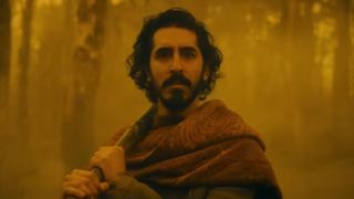 Dev Patel standing amidst an orange background in The Green Knight