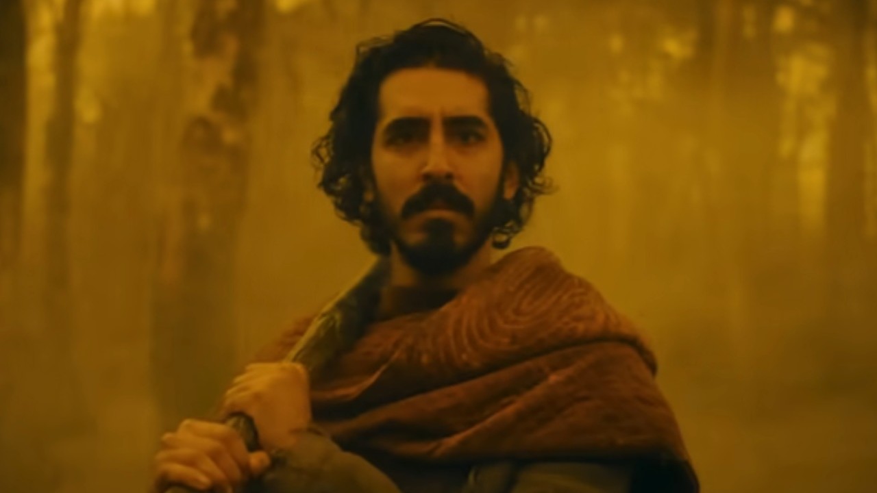 Dev Patel standing amidst an orange background in The Green Knight