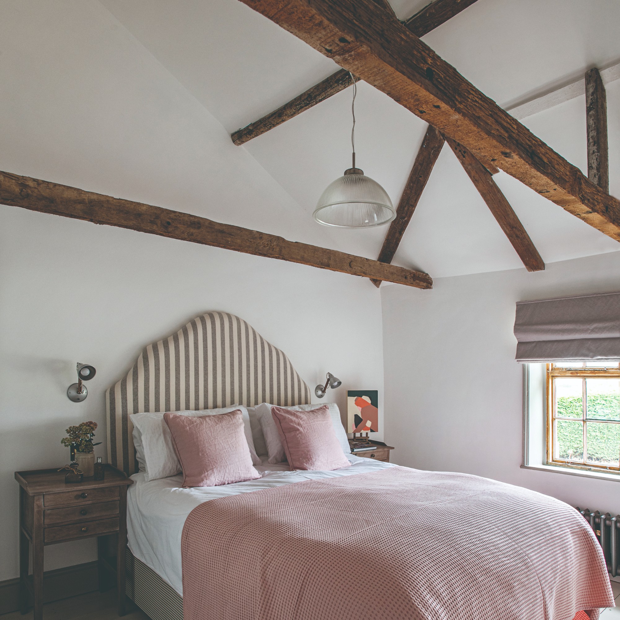 A white bedroom with exposed beam and a bed with a statement striped upholstered headboard