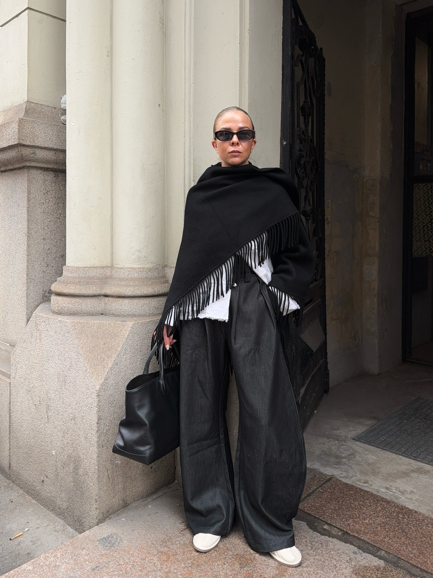 Woman wearing gray pants and black fringe scarf coat.