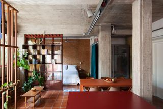 Athens Apartment by Point Supreme featuring a red tile floor, orange tables, chairs, and four by five book shelf.