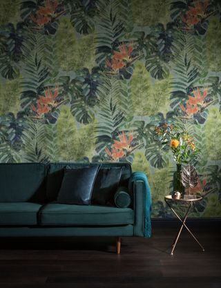 tropical leafy wallpaper in living room with pops of orange and greeny blue velvet sofa