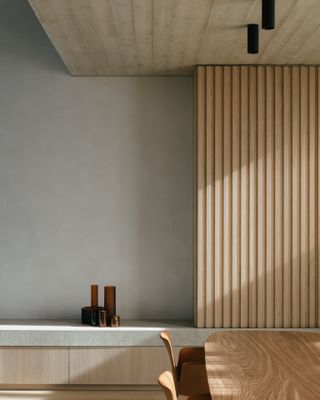 A dining area with a wooden table, a marble topped wall counter and wooden panels on a grey wall.