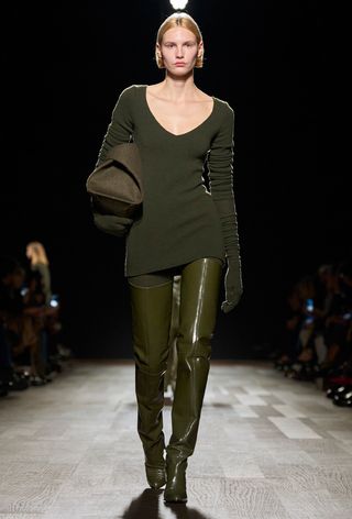 the best thigh-high boots on a model walking the Ferragamo runway show wearing an olive green knit dress with matching patent thigh-high heeled boots styled with a green hug bag