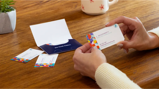 Two hands holding a VistaPrint business card on a desk