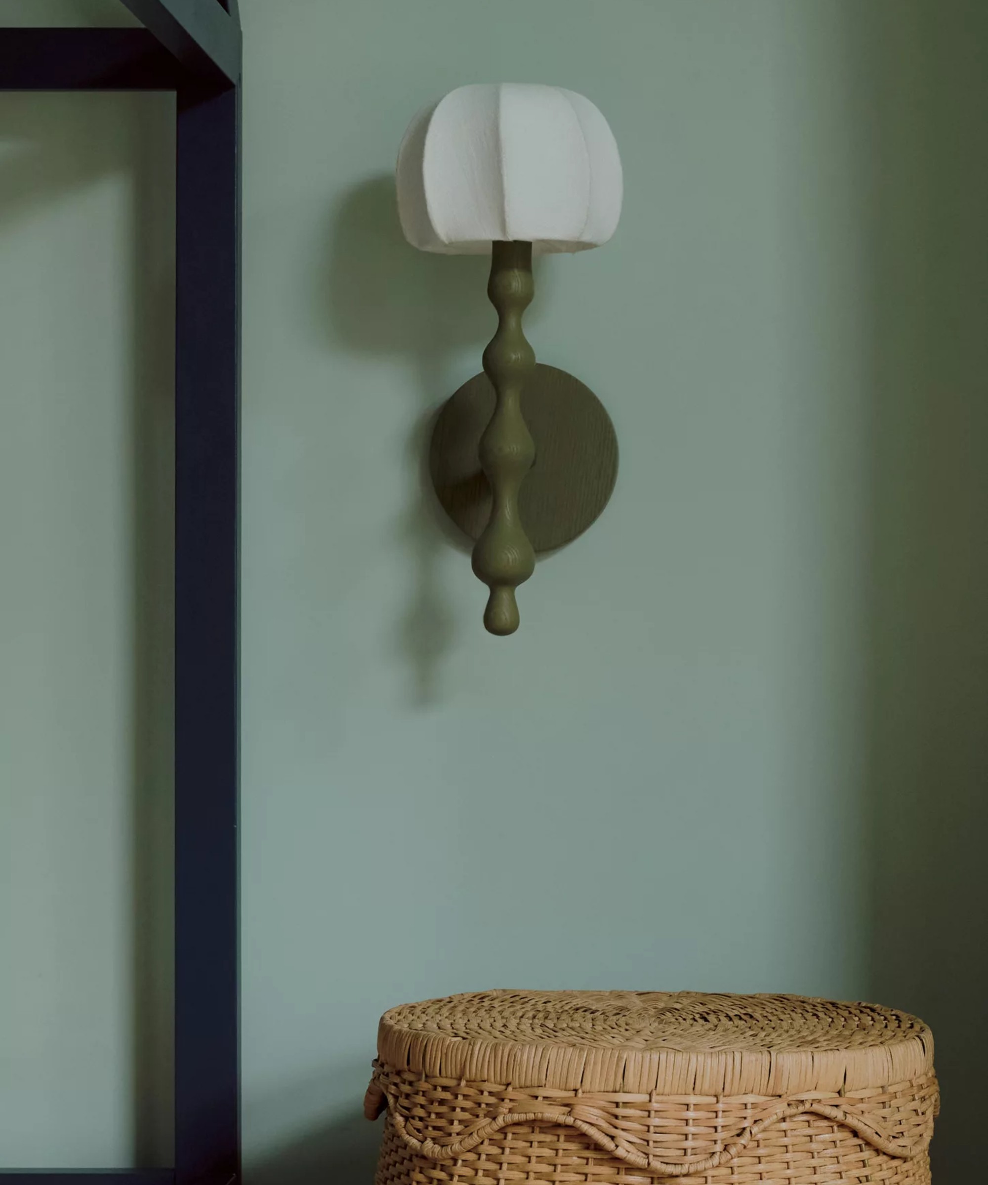 LALA Reimagined Wood Wall Light on a green wall with a wicker basket underneath