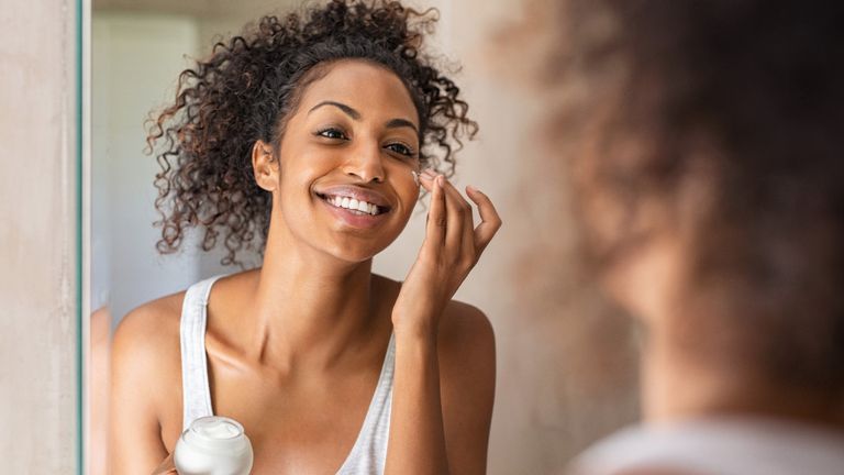 Woman applying eye cream and smiling in the mirror