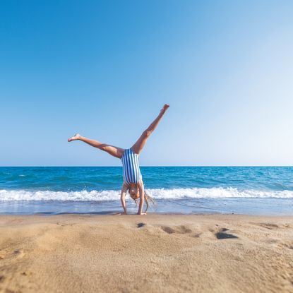 A child in a blue and white striped swimsuit doing a cartwheel on a beach