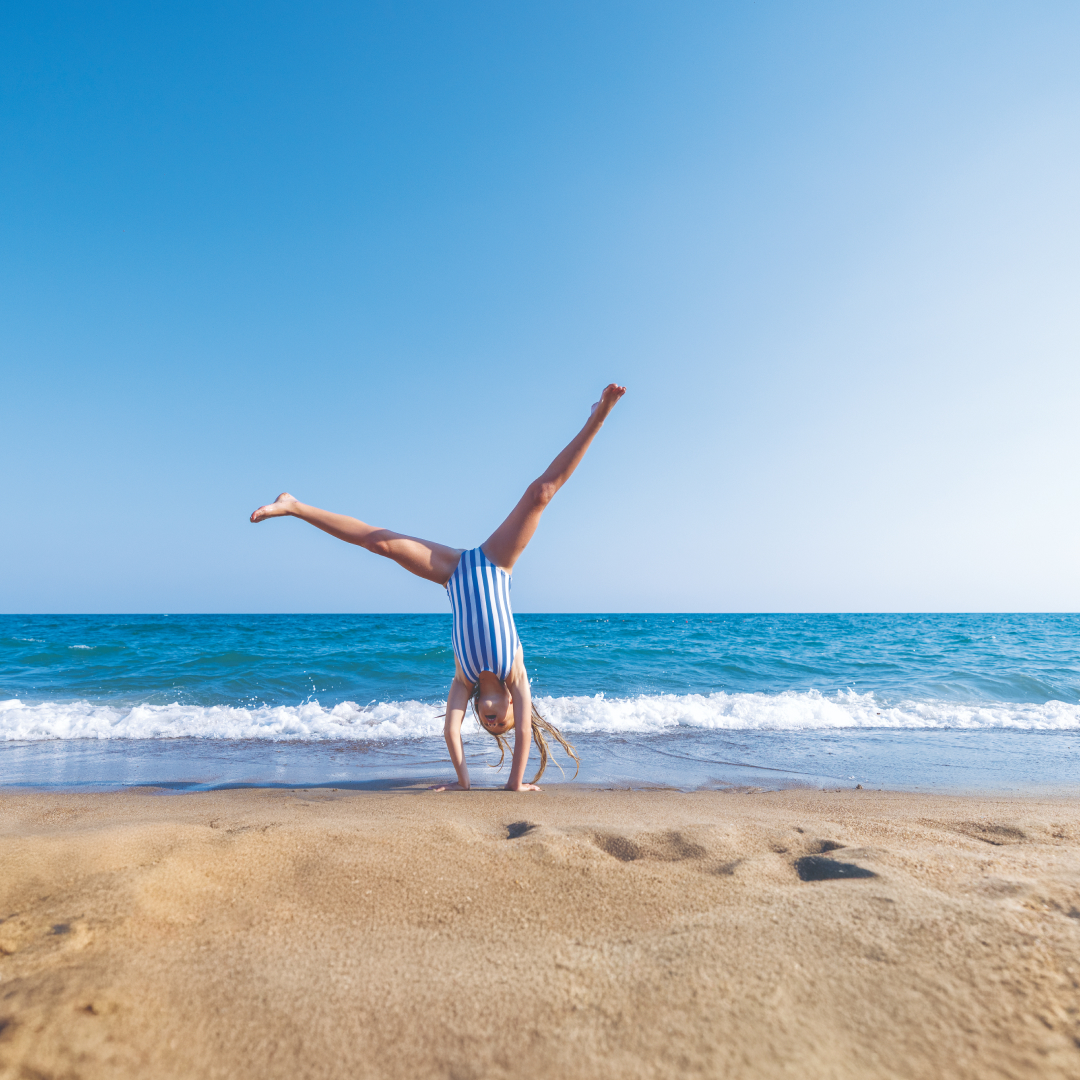 A child in a blue and white striped swimsuit doing a cartwheel on a beach