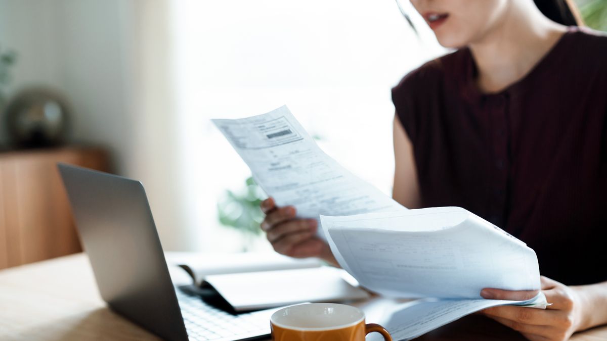 A woman looking through paper documentation in front of an open laptop