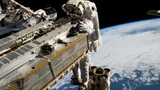 an astronaut floats above earth, holding a large metal space component.