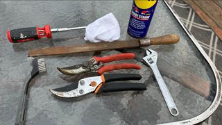 The tools required to sharpen bypass pruning shears, including a wrench, screwdriver, file, whetstone and brush
