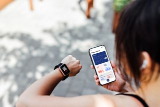 A woman using a fitness tracker app on her smart watch and her phone.