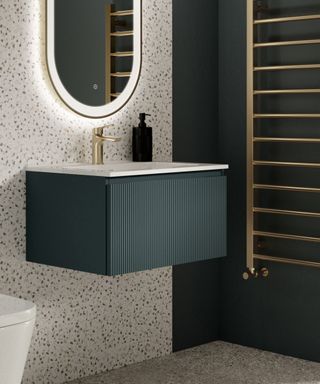 A contemporary bathroom vanity setup. The wall-mounted unit features a dark green, vertically ribbed cabinet beneath a pristine white countertop and integrated basin.