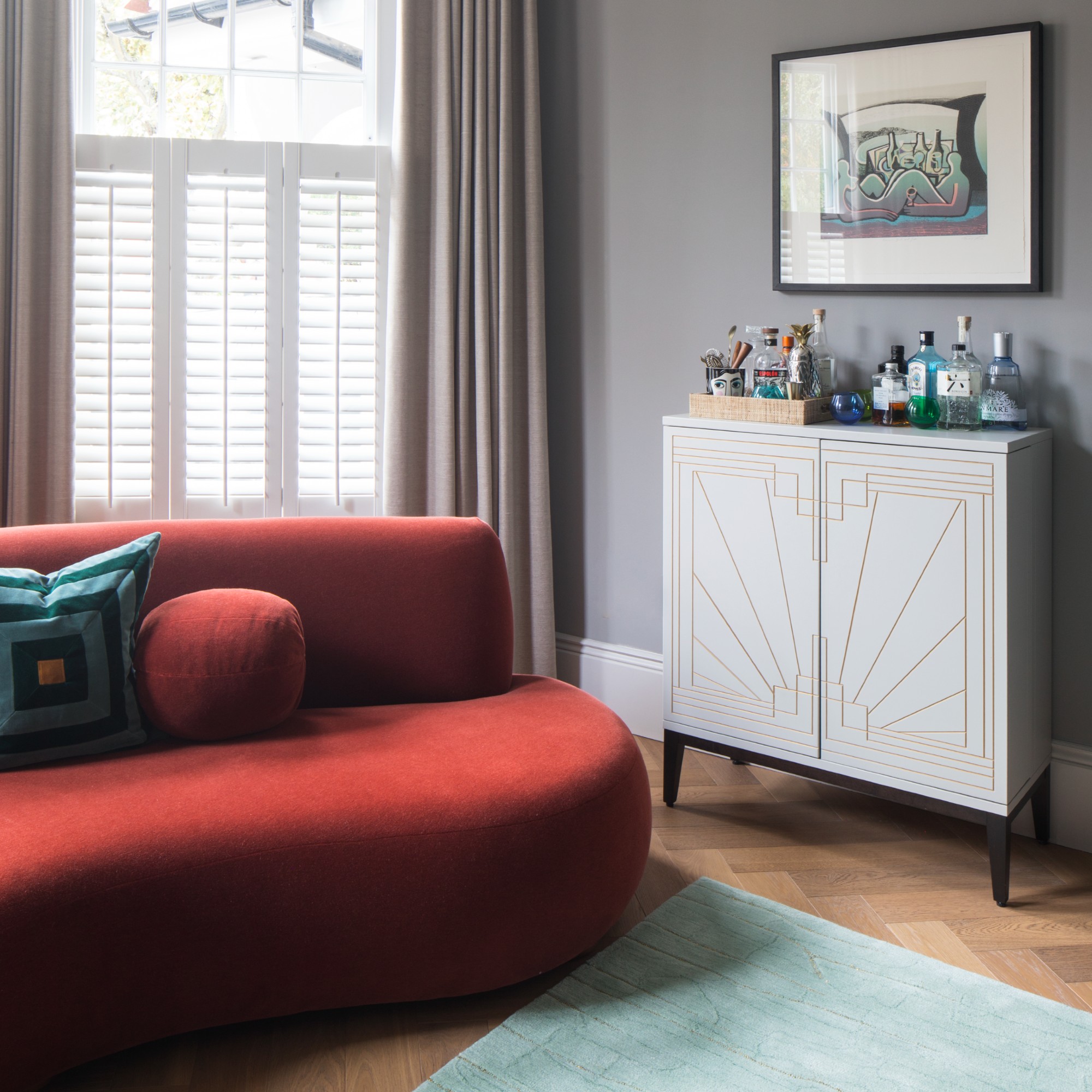 A grey living room with a curved red sofa and an eau de nile rug