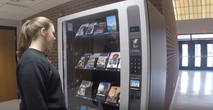 A student looks at a vending machine filled with books.