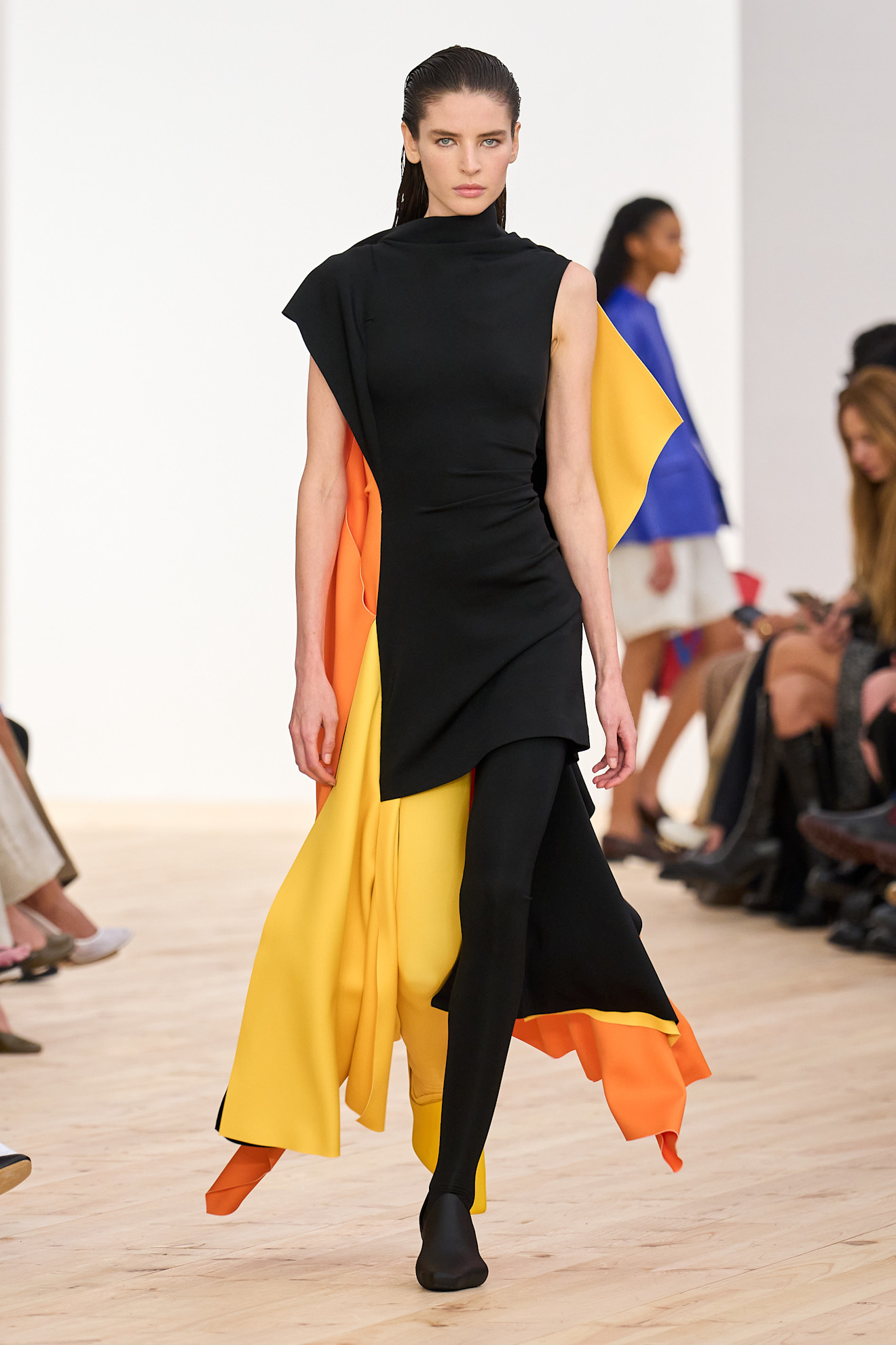 A model walking in the SS26 Loewe show is wearing a black, orange, and yellow dress.