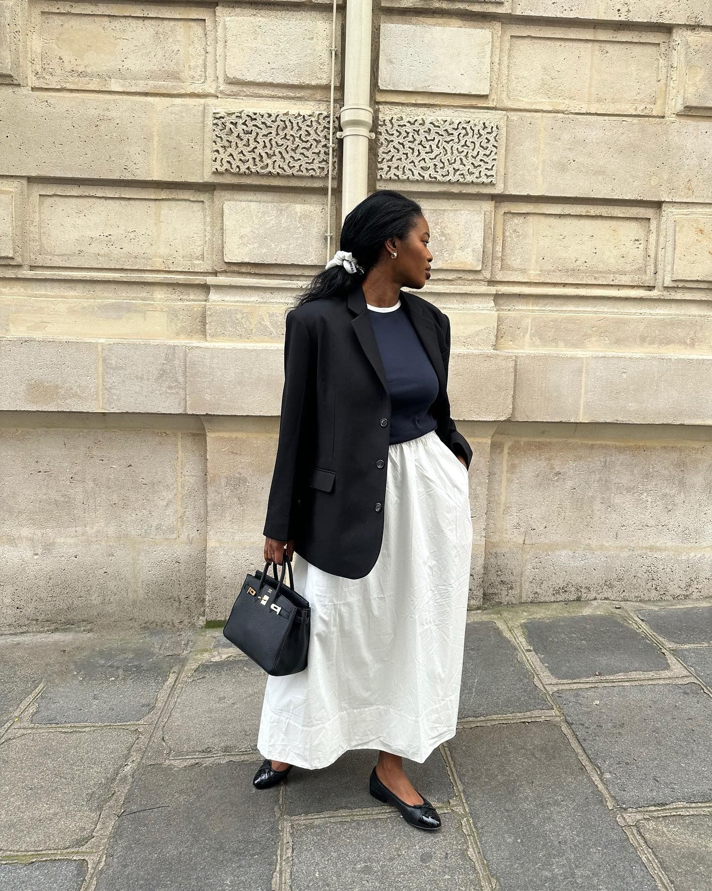 Influencer @nlmarilynwears a white skirt with black ballet flats, a black blazer and a navy knit.