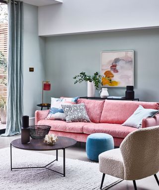 Living room of pink sofa and colourful cushions plus textured rug and full length curtains