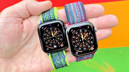 Close-up of the Apple Watch SE 3 and Apple Watch Series 11 in a user's hand with a colorful, out-of-focus background