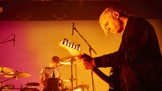Everything Everything guitarist live on stage bathed in orange light