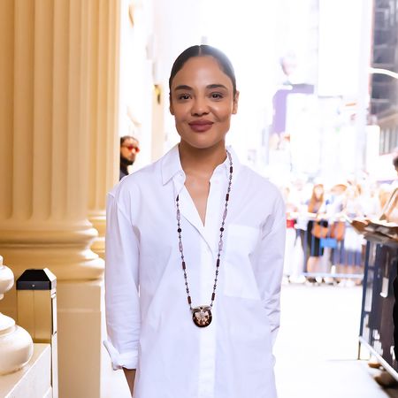 Tessa Thompson wearing a white button-dwon, black capri leggings, and purple mule heels