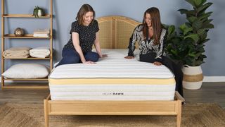 Two members of our testing team sit on top of the Helix Dawn mattress, our favorite mattress for stomach sleepers, on a bed frame in a bedroom